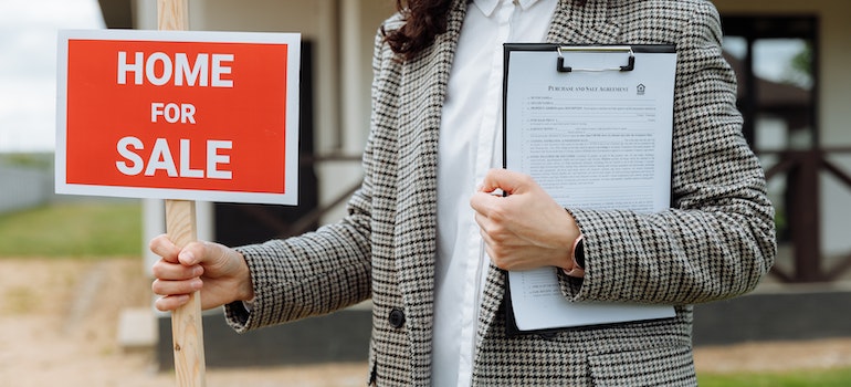 A woman holding a HOME FOR SALE sign